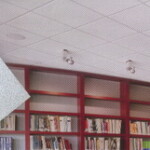 Armstrong DUNE 系列天花板安裝實景，搭配圖書館紅色書櫃牆面與曲線嵌燈天花板設計，展現現代商業空間的吸音與美觀兼具。